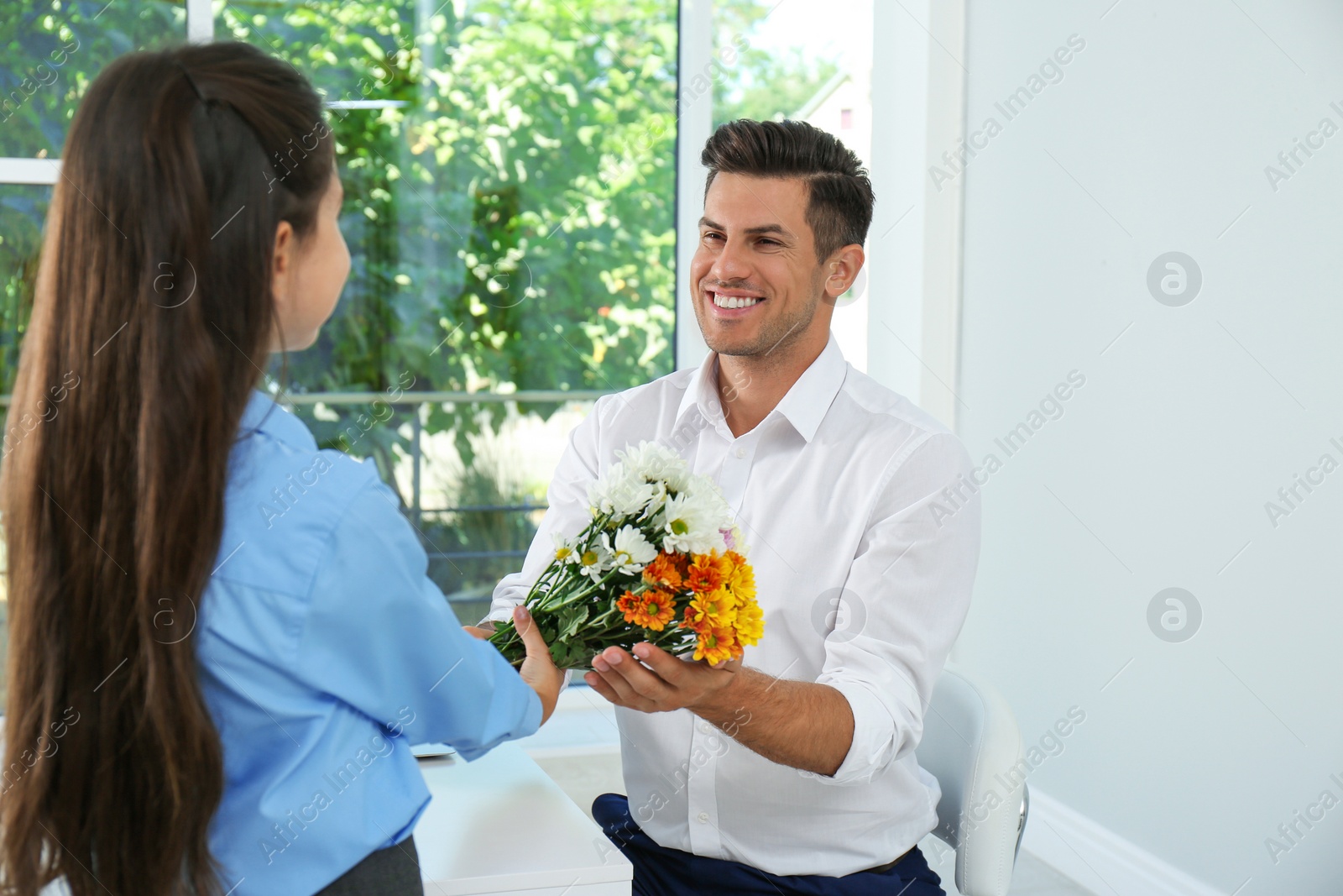 Photo of Schoolgirl congratulating her pedagogue with bouquet in classroom. Teacher's day