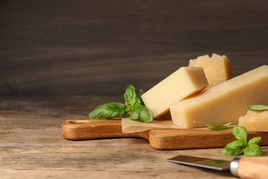 Photo of Delicious parmesan cheese with basil and knife on wooden table. Space for text
