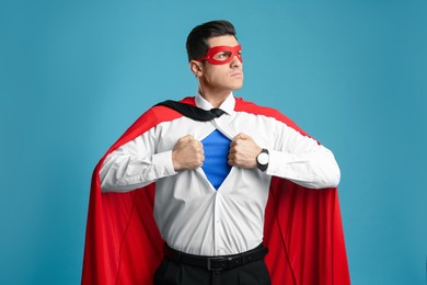 Photo of Businessman in superhero cape and mask taking shirt off on light blue background