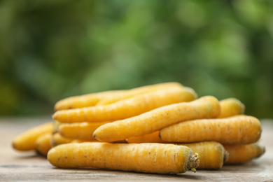 Photo of Raw yellow carrots on wooden table against blurred background