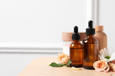 Bottles of cosmetic serum, beauty products and flowers on wooden table, space for text