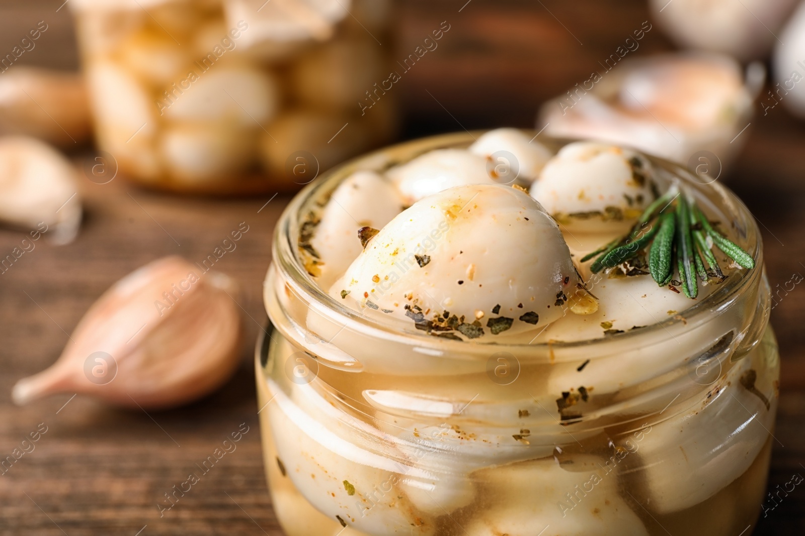 Photo of Preserved garlic in glass jar on wooden table, closeup