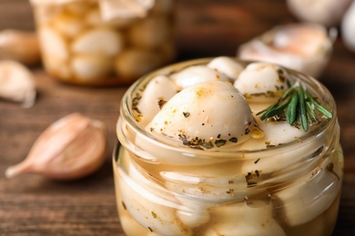 Photo of Preserved garlic in glass jar on wooden table, closeup