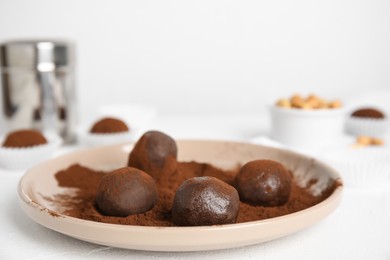 Photo of Plate with delicious chocolate truffles and cocoa powder on white table, closeup. Space for text