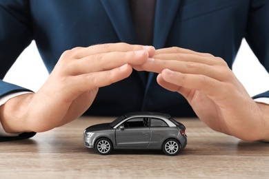 Photo of Insurance agent covering toy car on table, focus on hands