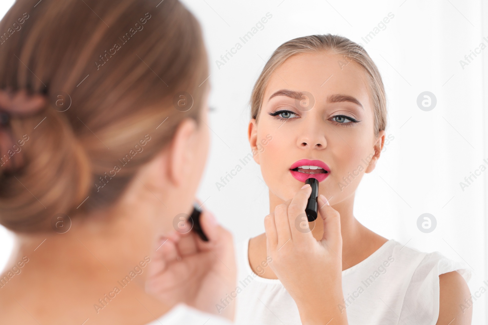 Photo of Beautiful young woman applying lipstick in front of mirror