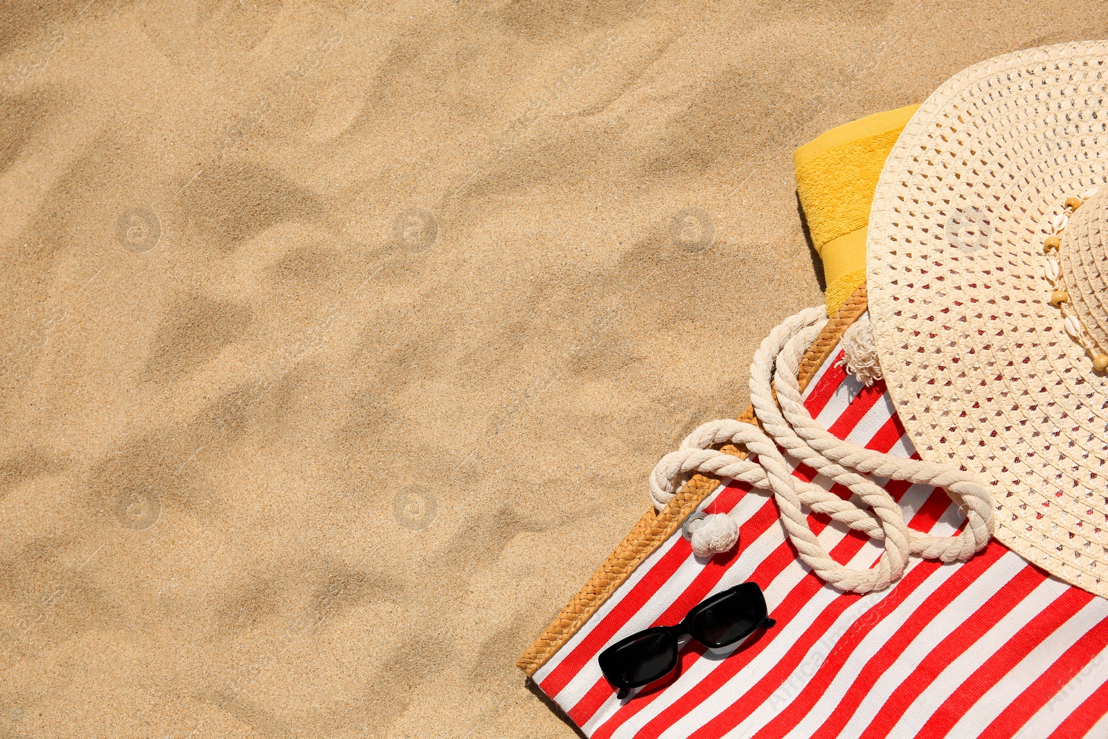 Photo of Striped beach bag, sunglasses, towel and hat on sand, flat lay. Space for text