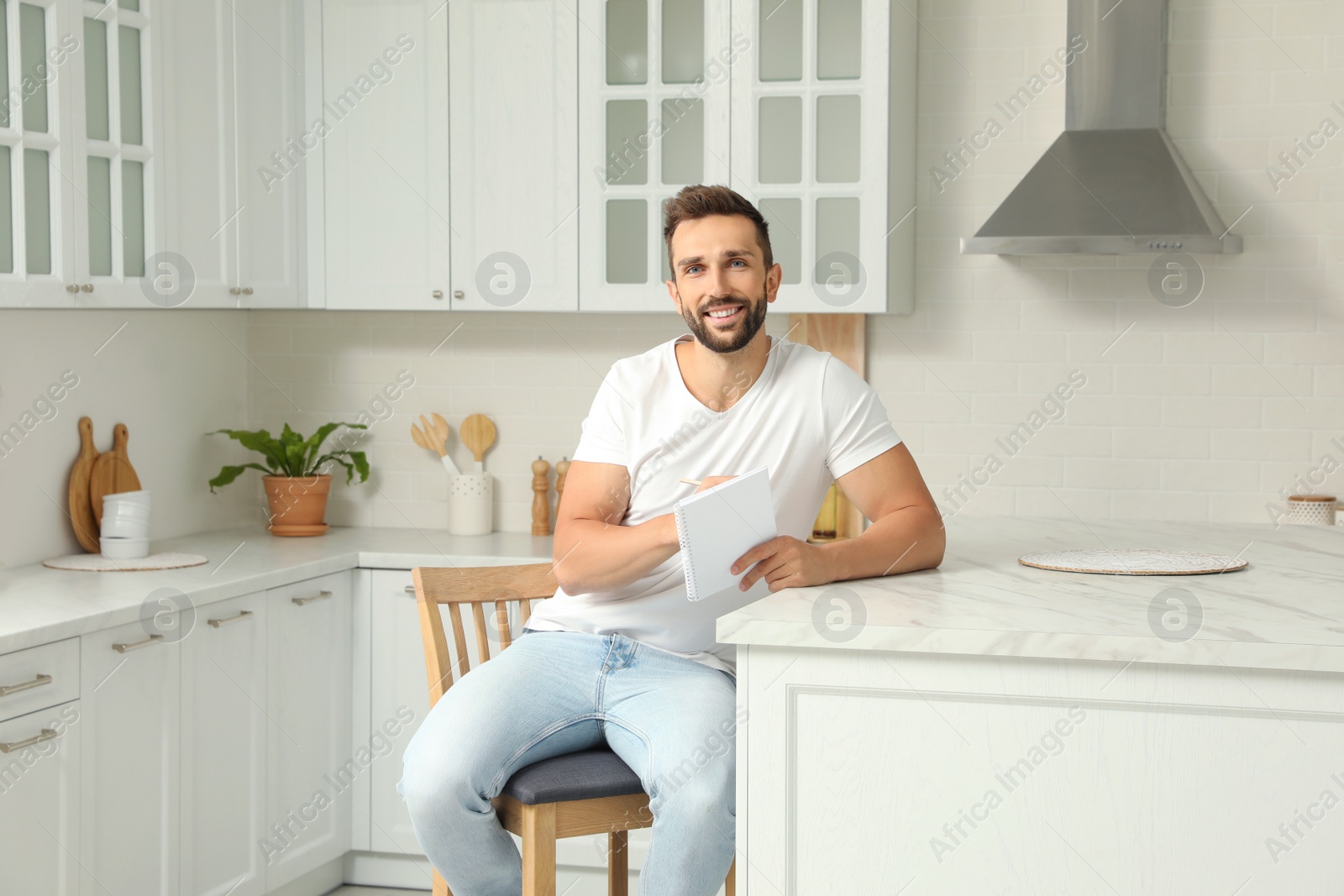 Photo of Handsome man with notebook sitting on stool in kitchen