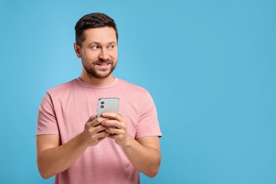 Man sending message via smartphone on light blue background, space for text