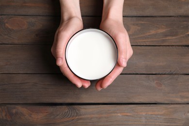 Photo of Woman holding glass of milk at wooden table, top view