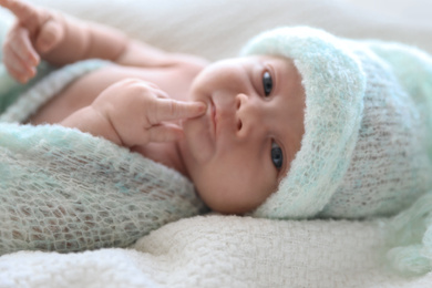 Cute newborn baby in warm hat lying on white plaid, closeup