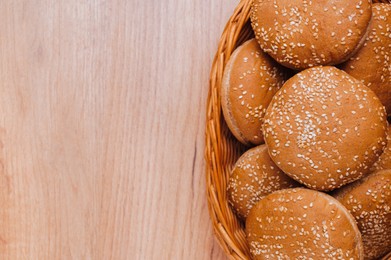 Photo of Wicker basket of fresh buns with sesame seeds on wooden table, top view. Space for text