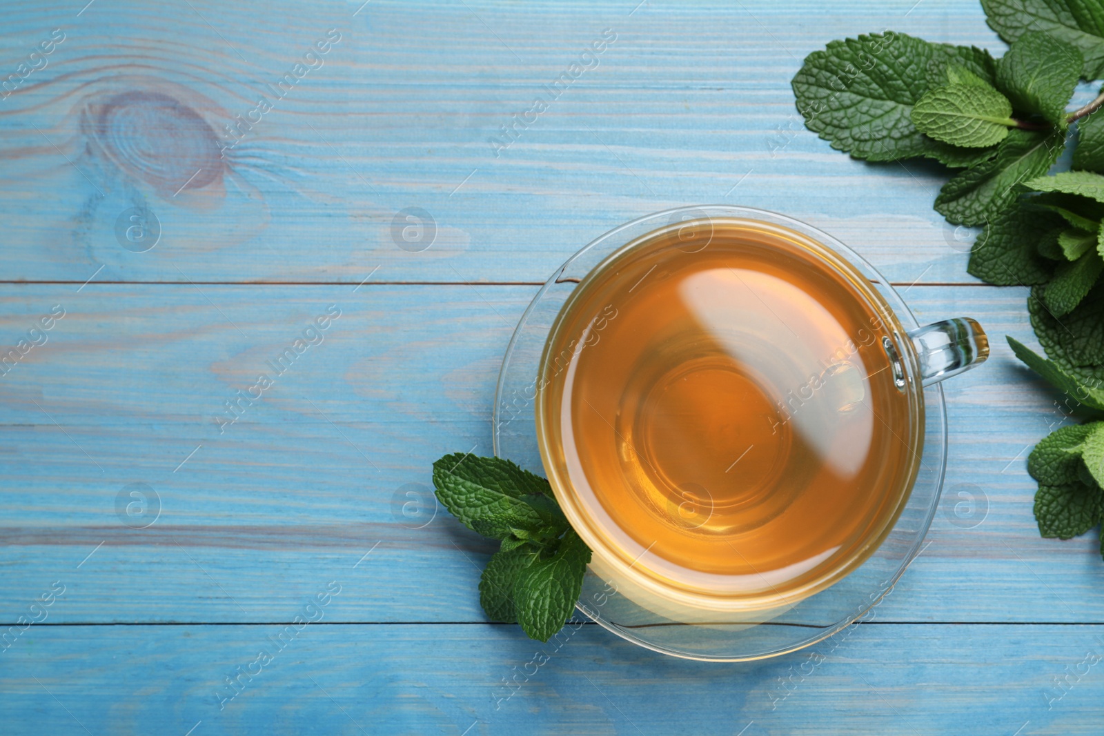 Photo of Cup of hot aromatic mint tea on light blue wooden table, flat lay. Space for text