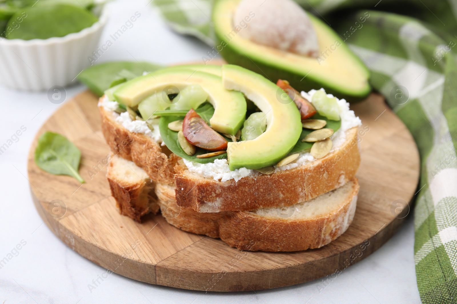 Photo of Tasty vegan sandwich with avocado, tomato and spinach on white marble table, closeup