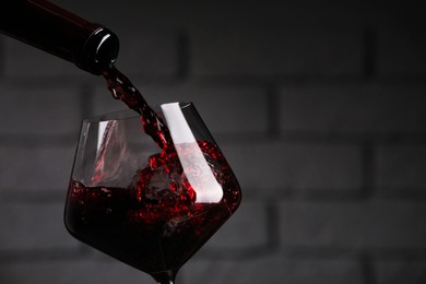 Photo of Pouring tasty red wine from bottle into glass against brick wall, closeup. Space for text