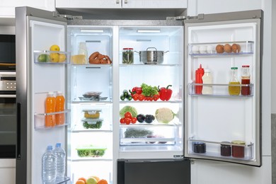 Modern open refrigerator full of different products in kitchen