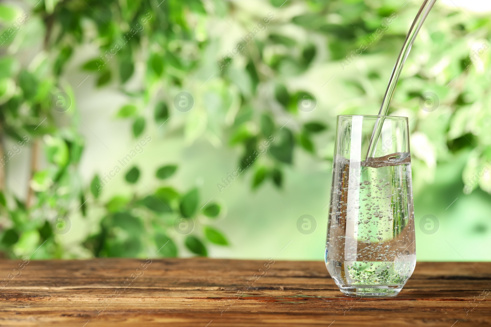 Photo of Pouring water into glass on wooden table outdoors, space for text. Refreshing drink