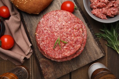 Photo of Raw hamburger patties with rosemary and tomatoes on wooden table, flat lay