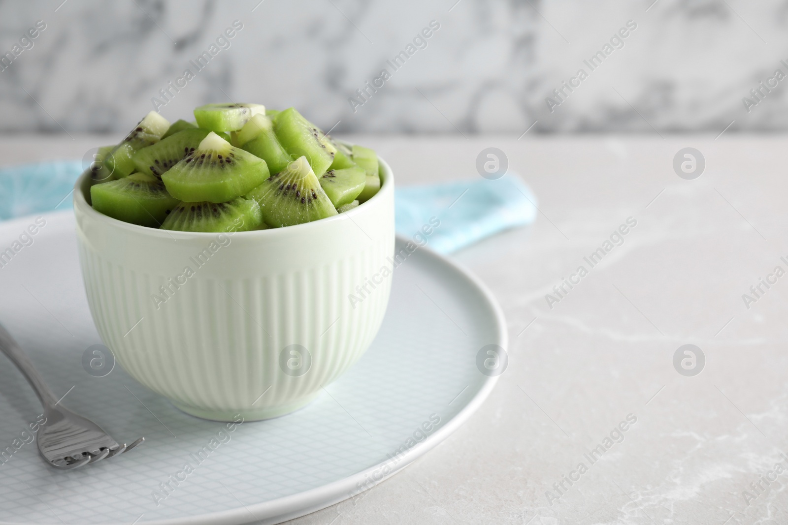 Photo of Bowl with kiwi slices on light grey marble table. Space for text