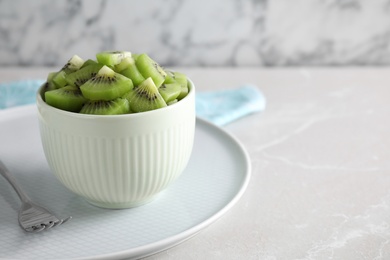 Photo of Bowl with kiwi slices on light grey marble table. Space for text