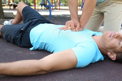 Passerby performing CPR on unconscious man outdoors. First aid