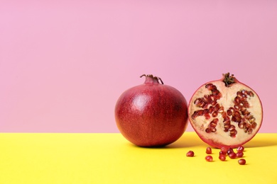 Photo of Delicious red ripe pomegranates on table against color background, space for text