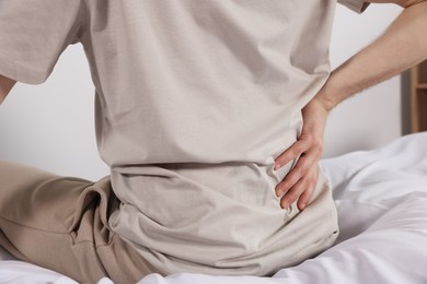 Photo of Man suffering from back pain while sitting on bed indoors, closeup. Symptom of scoliosis