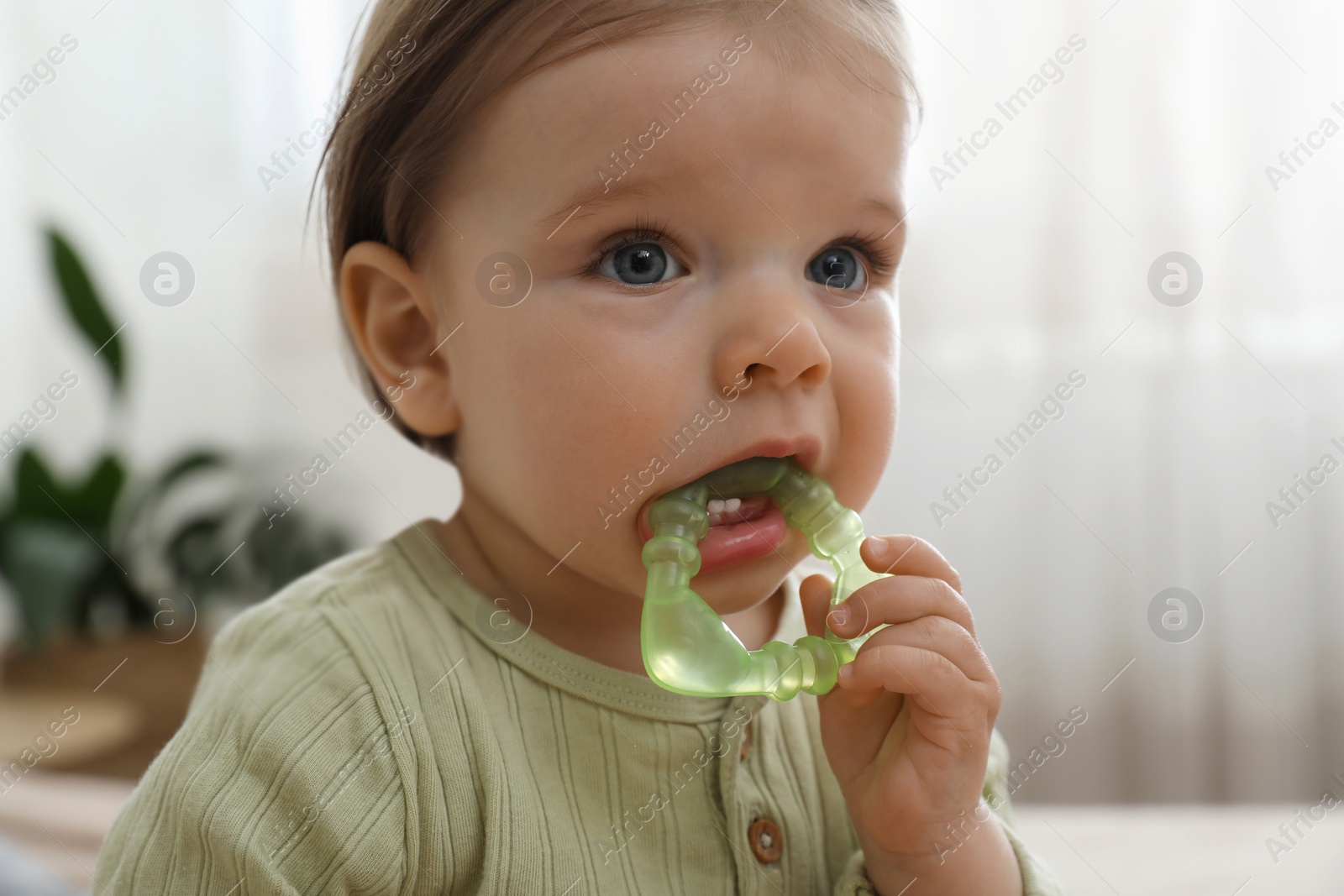 Photo of Cute baby girl with teething toy at home, closeup