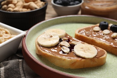 Photo of Toasts with tasty nut butter, banana slices, blueberries and peanuts on table, closeup