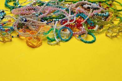 Photo of Pile of beautiful handmade beaded jewelry on yellow background. Space for text