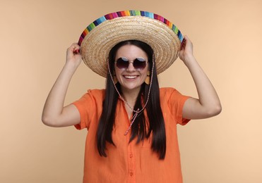 Young woman in Mexican sombrero hat and sunglasses on beige background