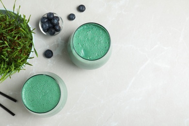 Photo of Flat lay composition with glasses of spirulina smoothie, wheat grass and blueberries on light background. Space for text