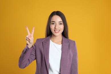 Photo of Woman in violet blazer showing number two with her hand on yellow background