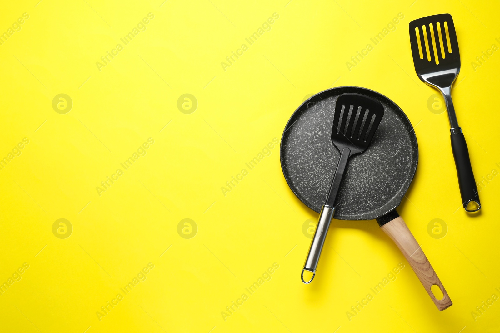 Photo of Spatulas and frying pan on yellow background, flat lay. Space for text