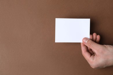 Photo of Man holding paper card on brown background, top view. Mockup for design