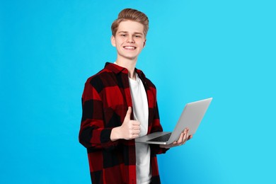 Photo of Teenage boy with laptop showing thumb up on light blue background