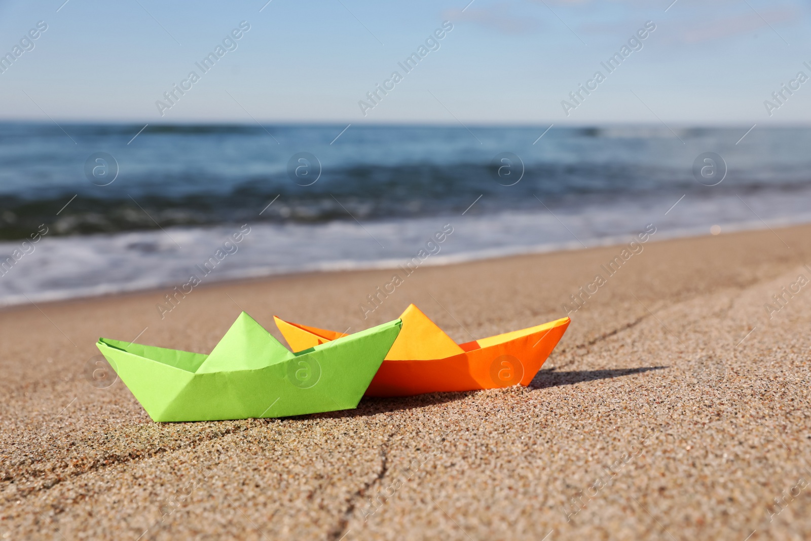 Photo of Bright color paper boats on sandy beach near sea