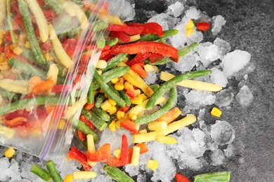 Photo of Zip bag with different frozen vegetables and ice on grey table, top view
