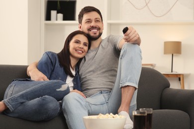 Happy couple watching show at home. Man changing TV channels with remote control