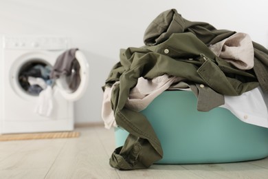 Photo of Laundry basket with clothes on floor near washing machine indoors