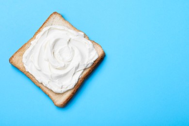 Photo of Slice of bread with tasty cream cheese on light blue background, top view. Space for text