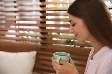 Photo of Beautiful young woman with cup of tea near window indoors