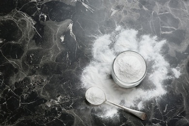 Photo of Jar and spoon with baking soda on grey background, top view. Space for text