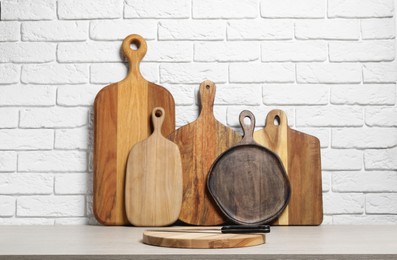 Photo of Different cutting boards and knife on light table near white brick wall