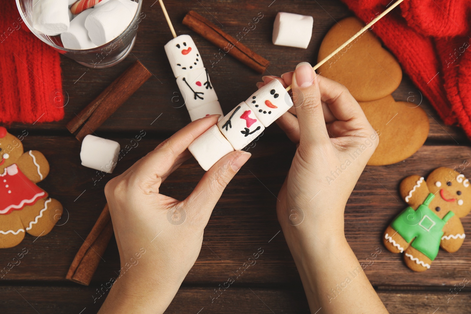 Photo of Woman making funny snowman with marshmallows at wooden table, top view