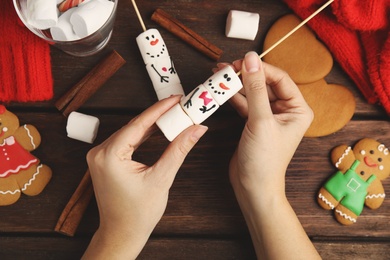 Woman making funny snowman with marshmallows at wooden table, top view