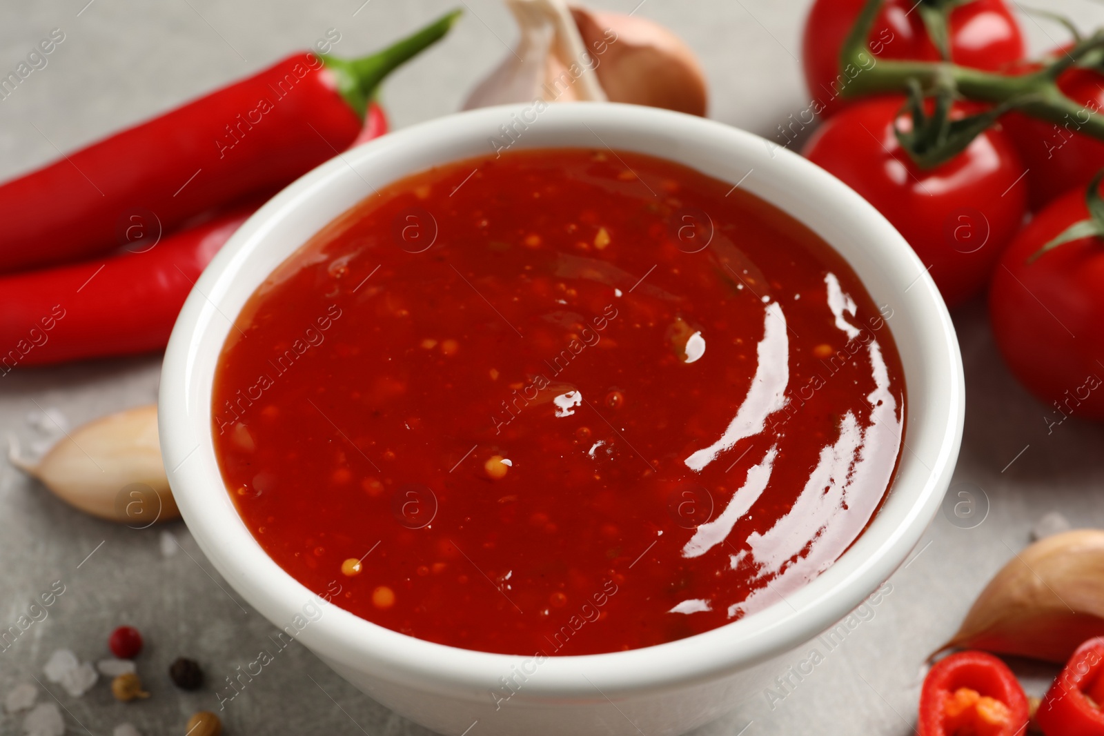 Photo of Spicy chili sauce in bowl on grey table, closeup