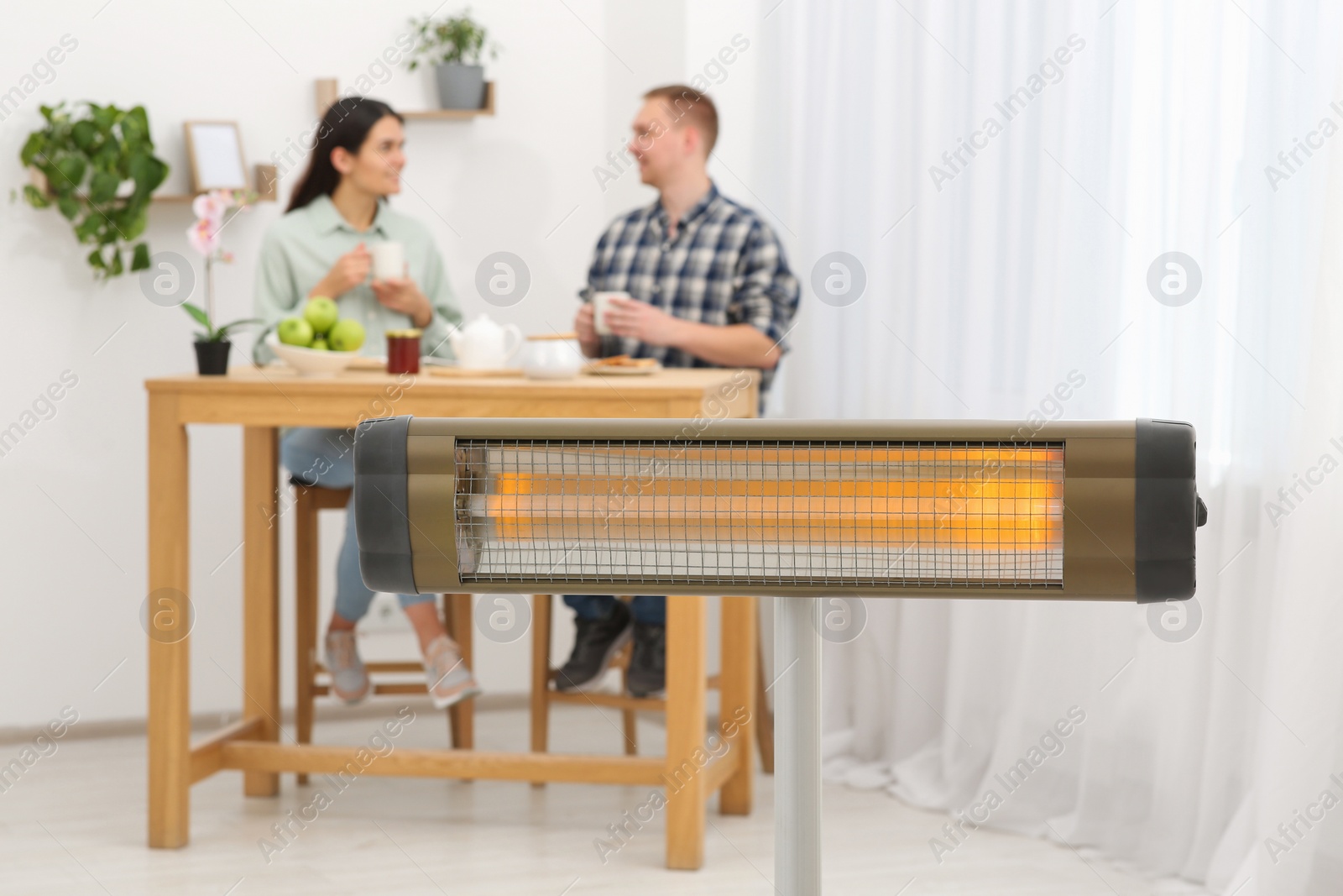 Photo of Couple spending time in room with modern electric infrared heater, focus on appliance