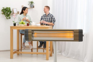 Couple spending time in room with modern electric infrared heater, focus on appliance