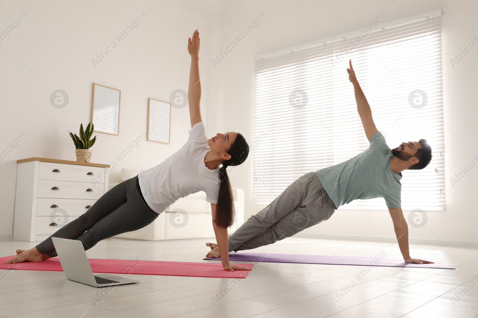 Photo of Couple practicing yoga while watching online class at home during coronavirus pandemic. Social distancing